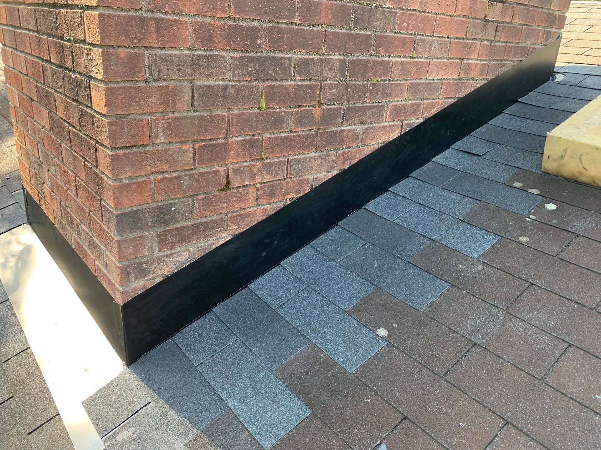 A brick chimney is sitting on top of a roof next to a brick wall.