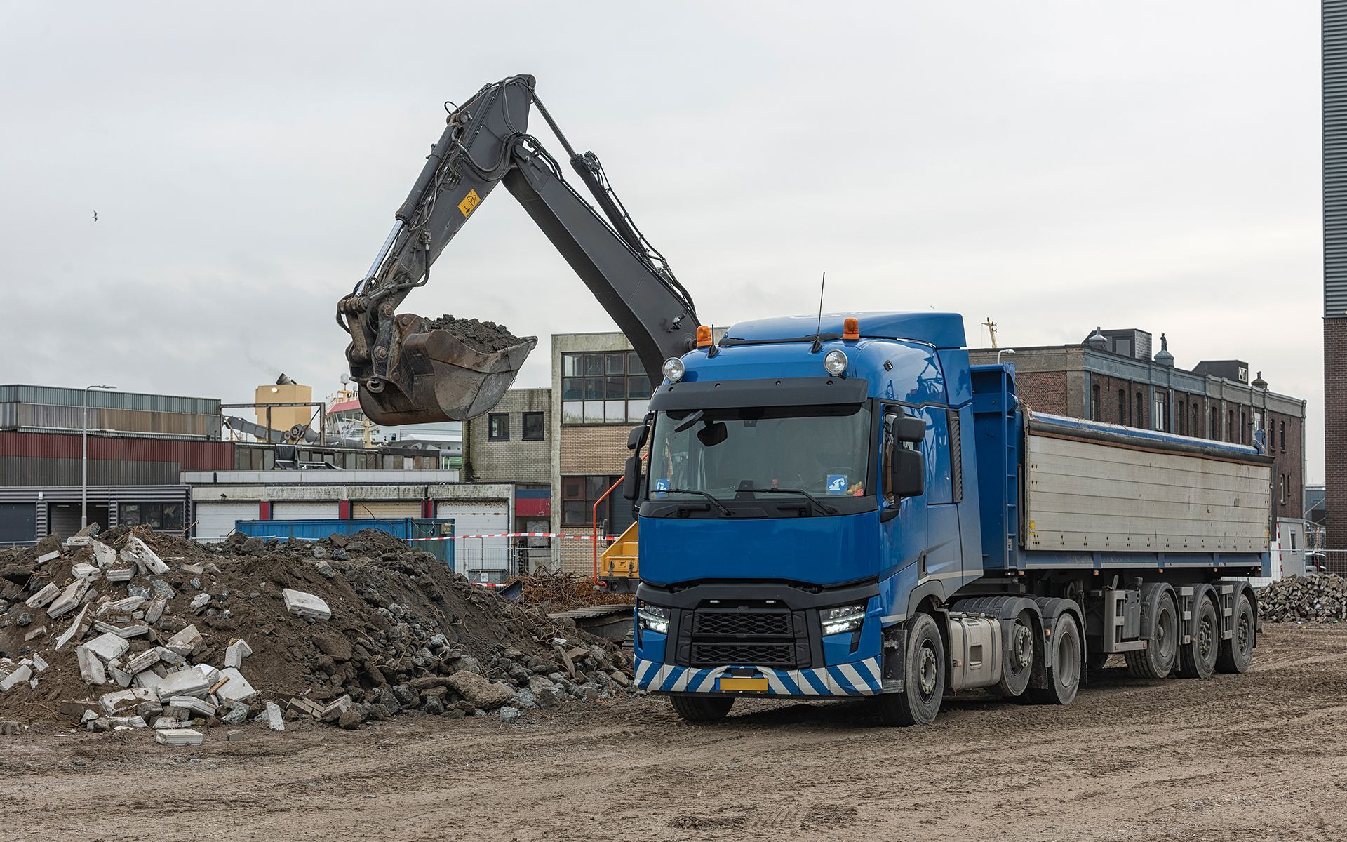 A blue dump truck is being loaded with dirt by an excavator.