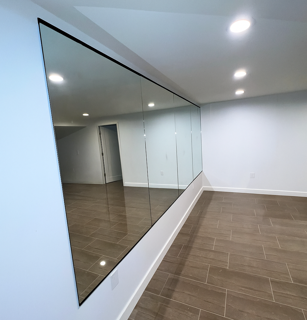 A room with a large wall mirror, white walls, and wood-look flooring.