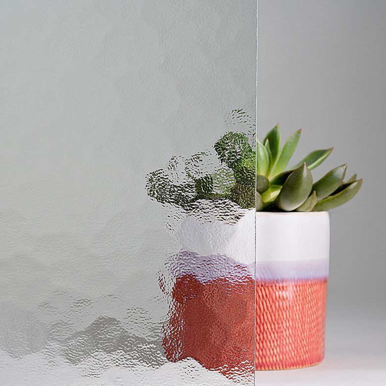 Textured glass pane beside a potted succulent against a light gray background.