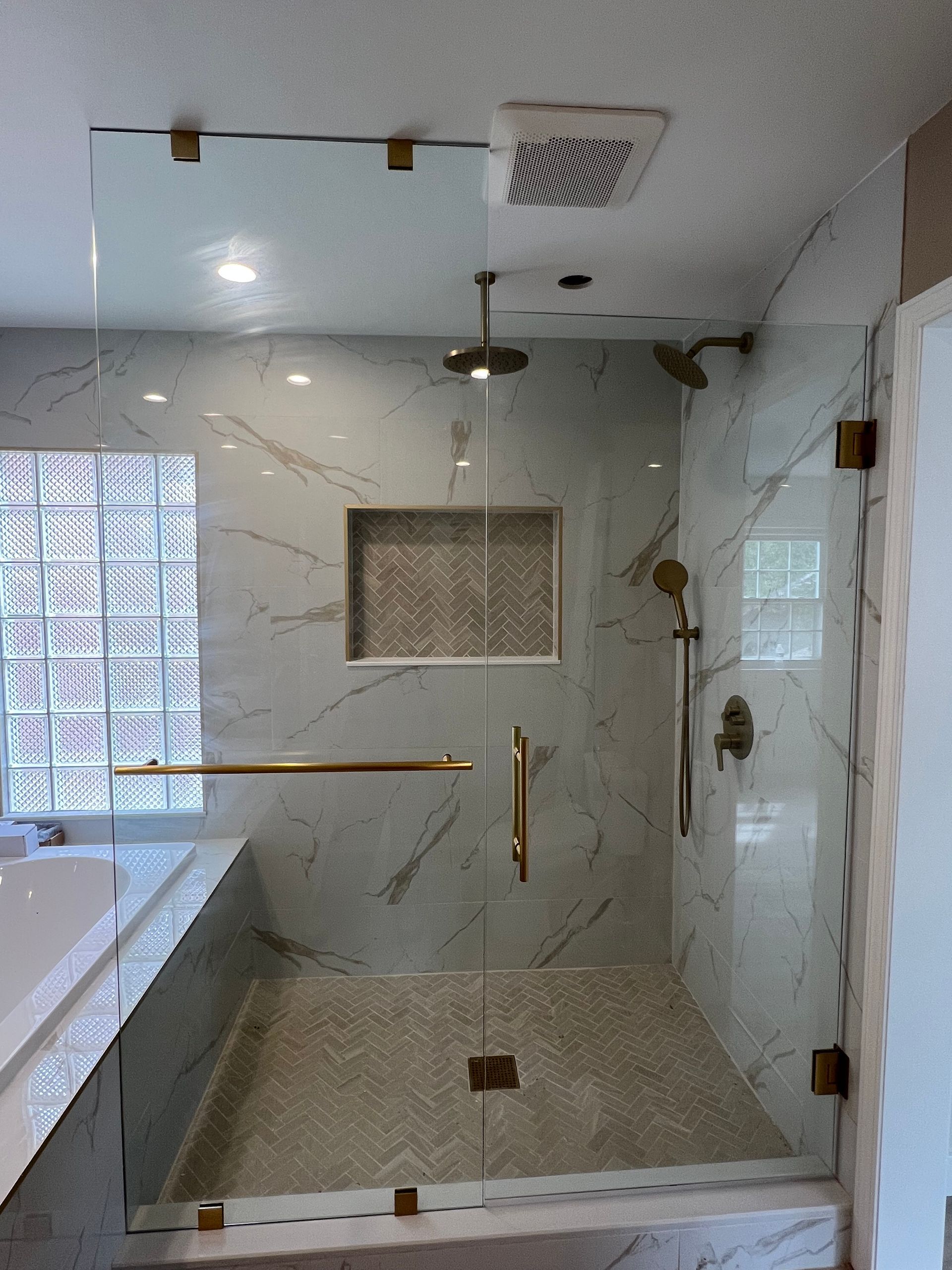 Glass shower with gold hardware, marble tile, and a recessed decorative tile niche. Dearborn