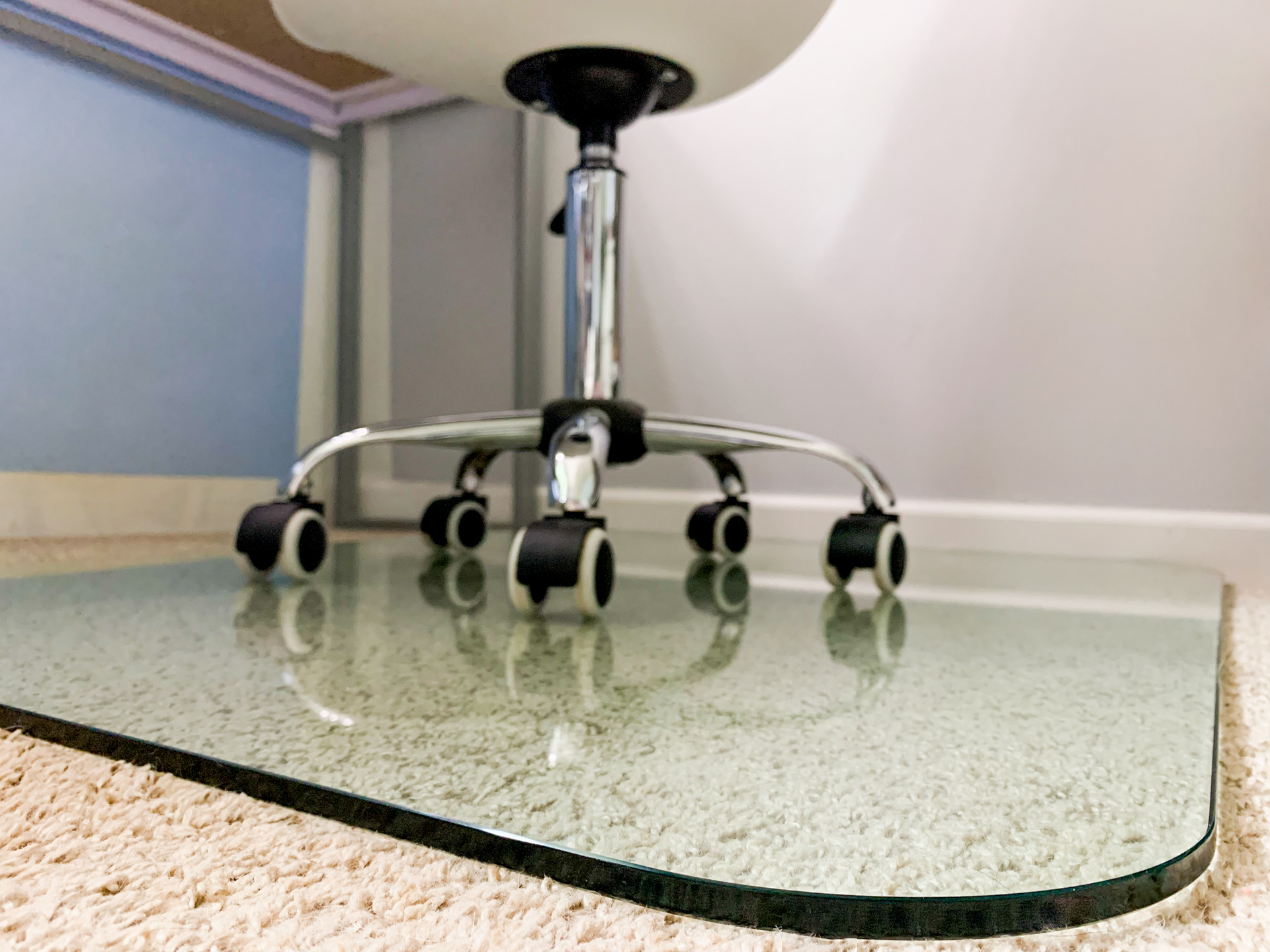 Clear glass chair mat on carpet, under a chrome office chair.