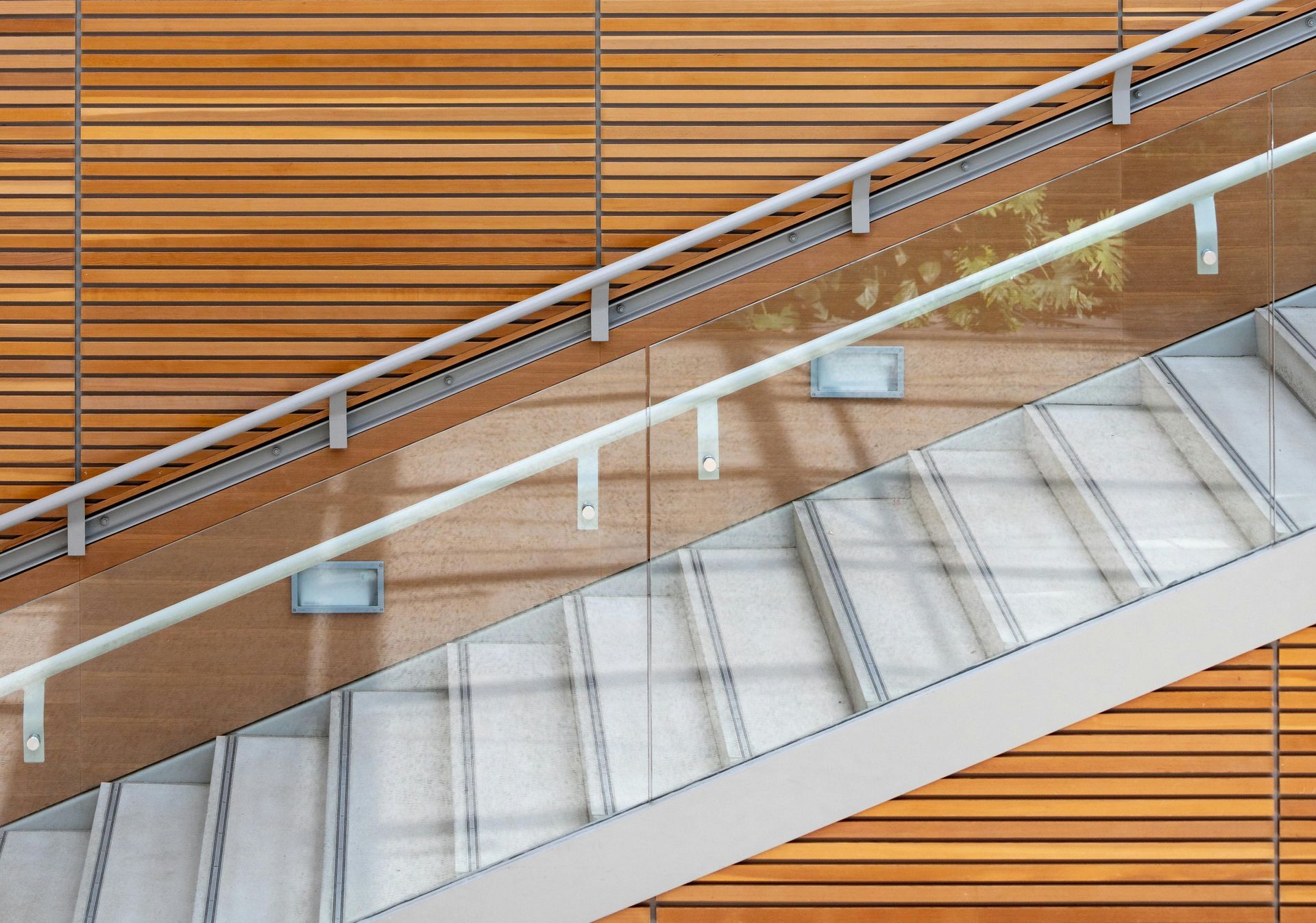 Staircase with white steps, glass panels, and a metal handrail, against a wooden wall.