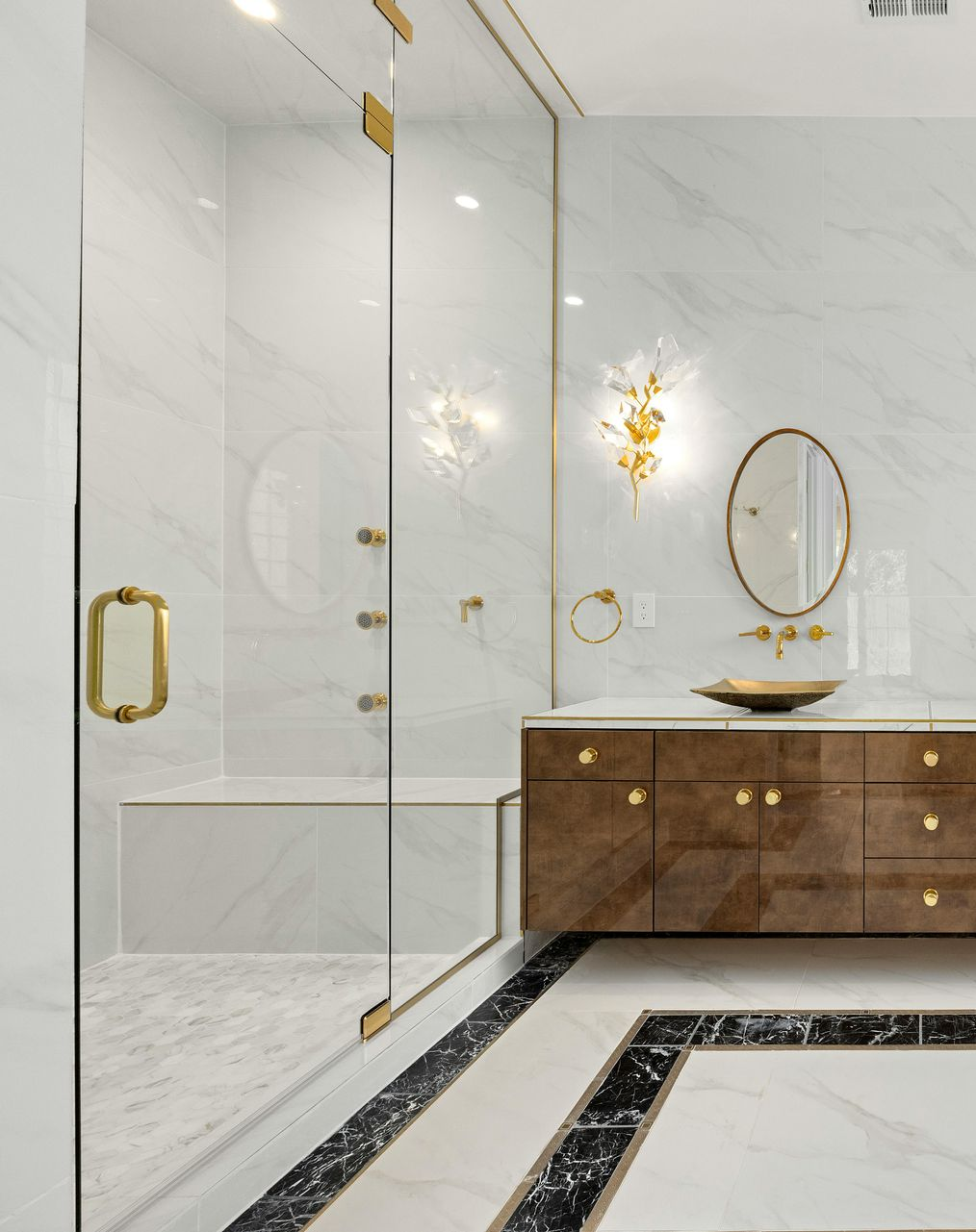 Luxurious bathroom with marble walls, glass shower, and gold accents.