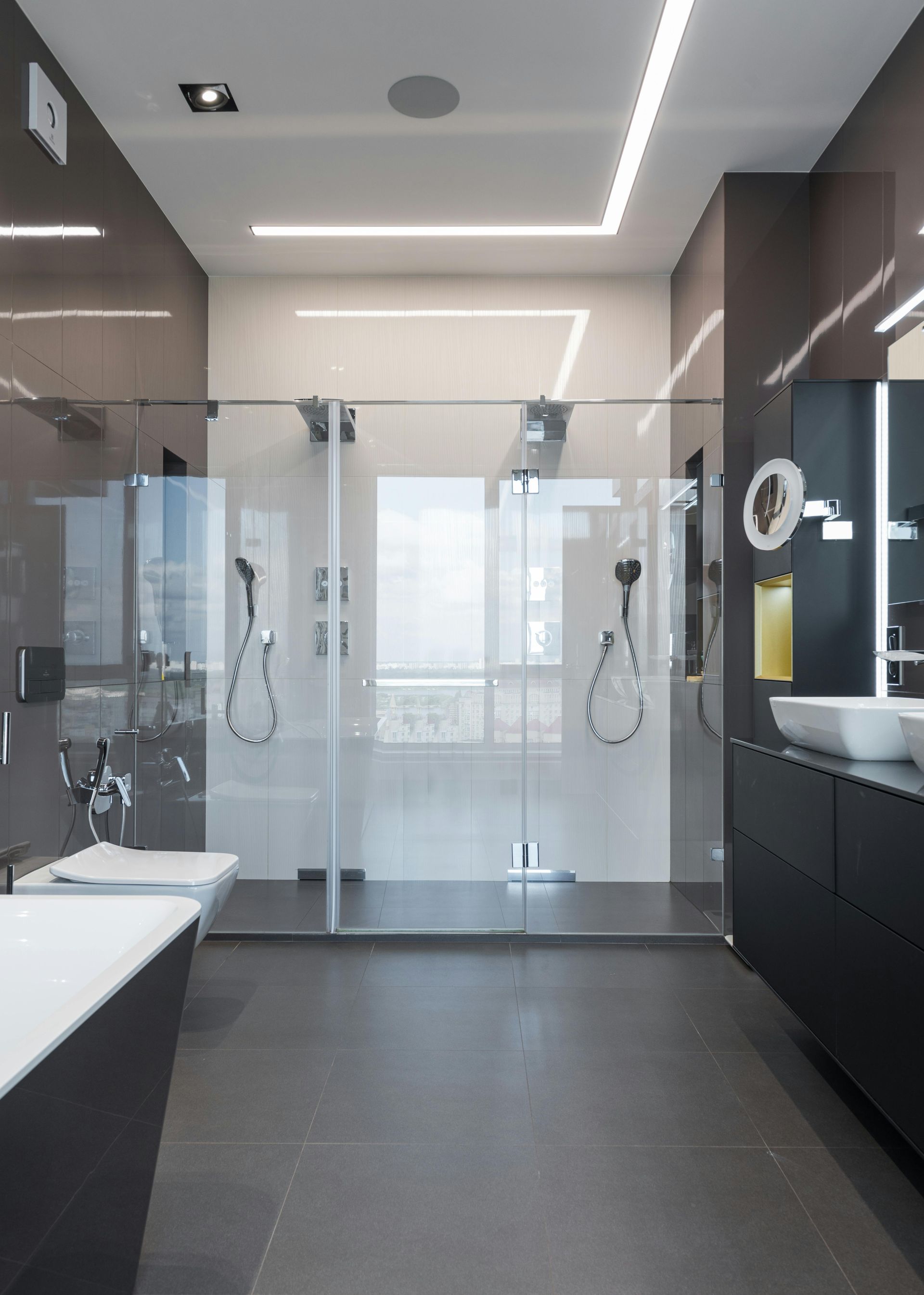Modern bathroom with a glass shower, dark gray tile, and two white sinks.