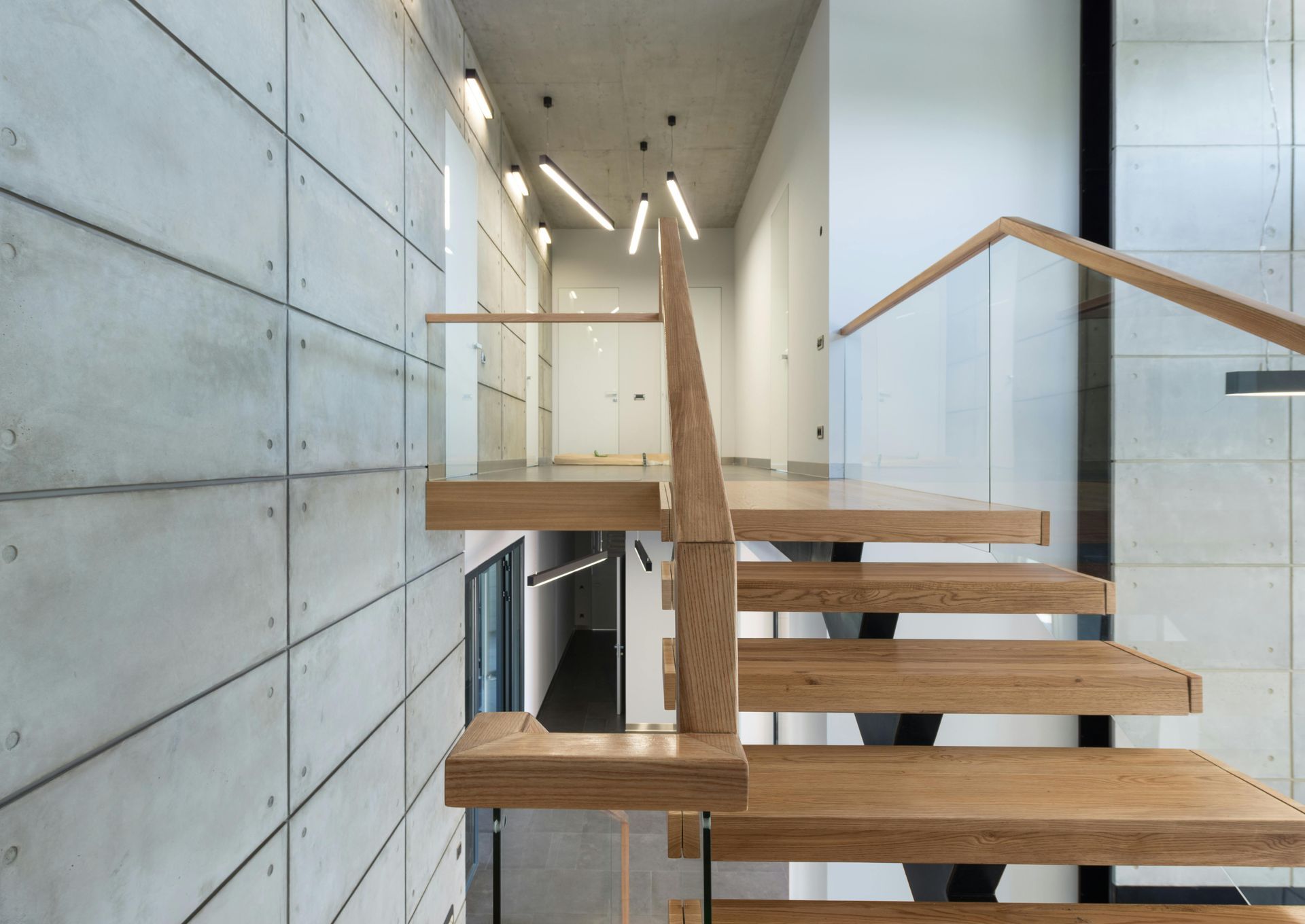 Wooden staircase with glass railing and concrete panel wall.