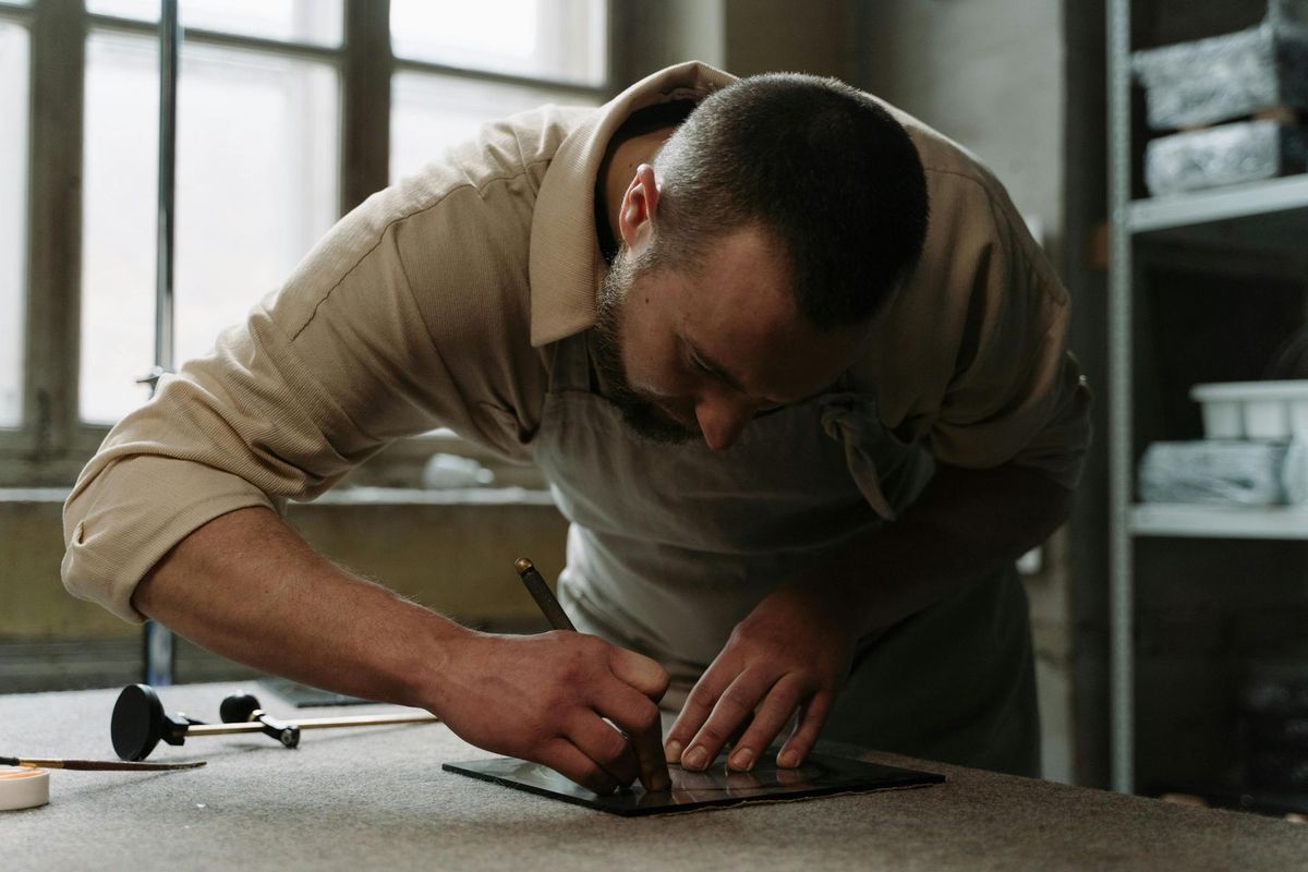 A person in a workshop scoring glass, bent over a table.