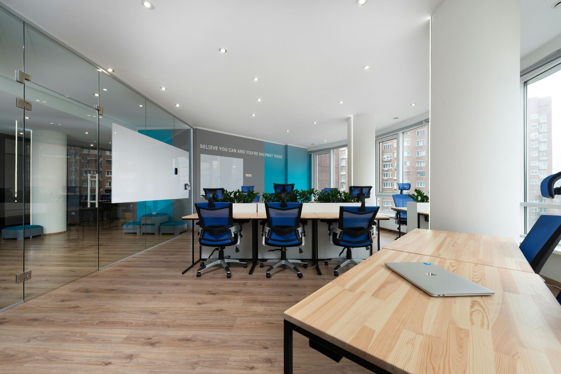 Modern office space with desks, blue chairs, glass walls, and a whiteboard.