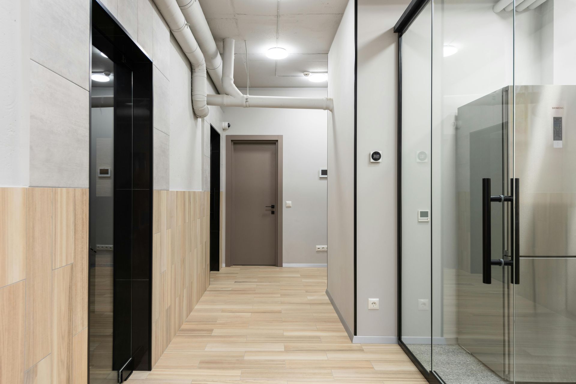 Hallway with wood floors, light wood paneling, gray walls, and glass-paneled refrigerator.