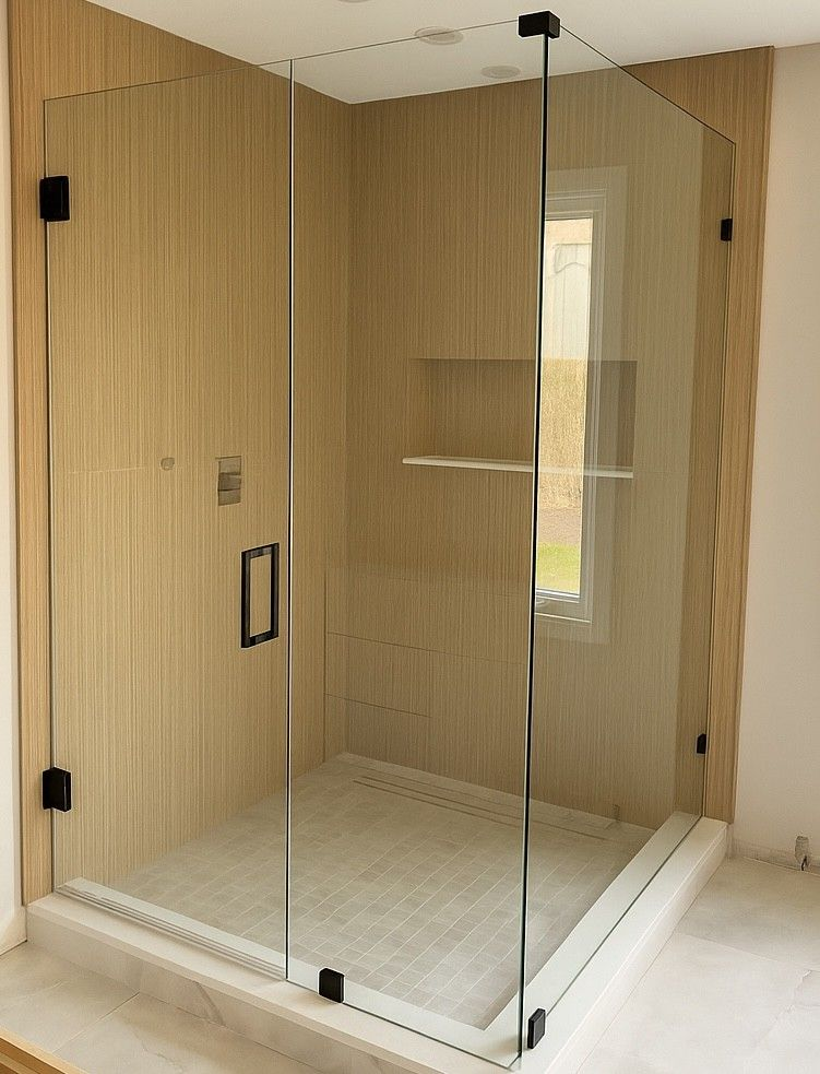 Glass shower enclosure with black hardware, beige tiled walls, and light-colored floor.