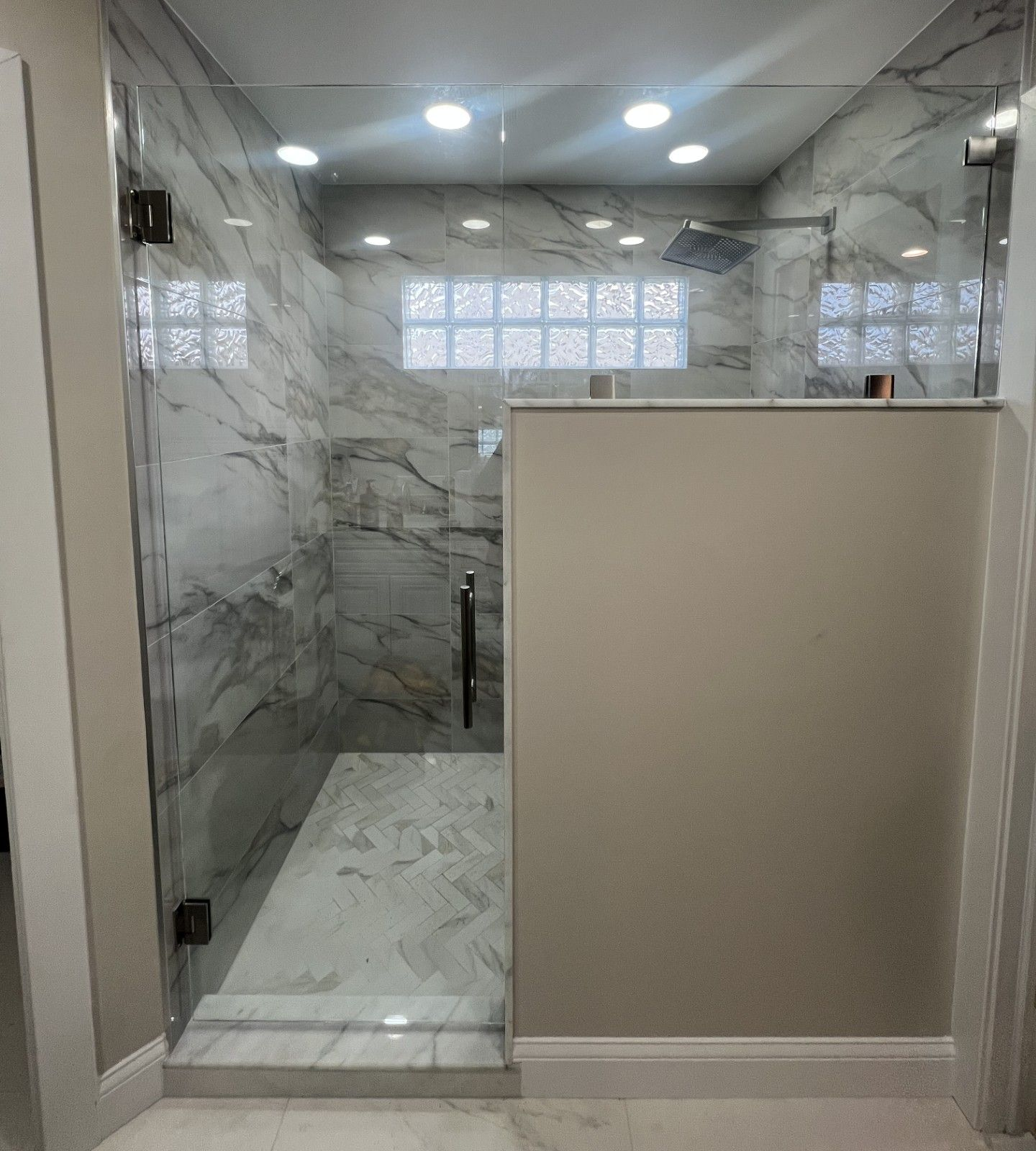 Modern shower with glass doors, marble tile, and neutral walls.