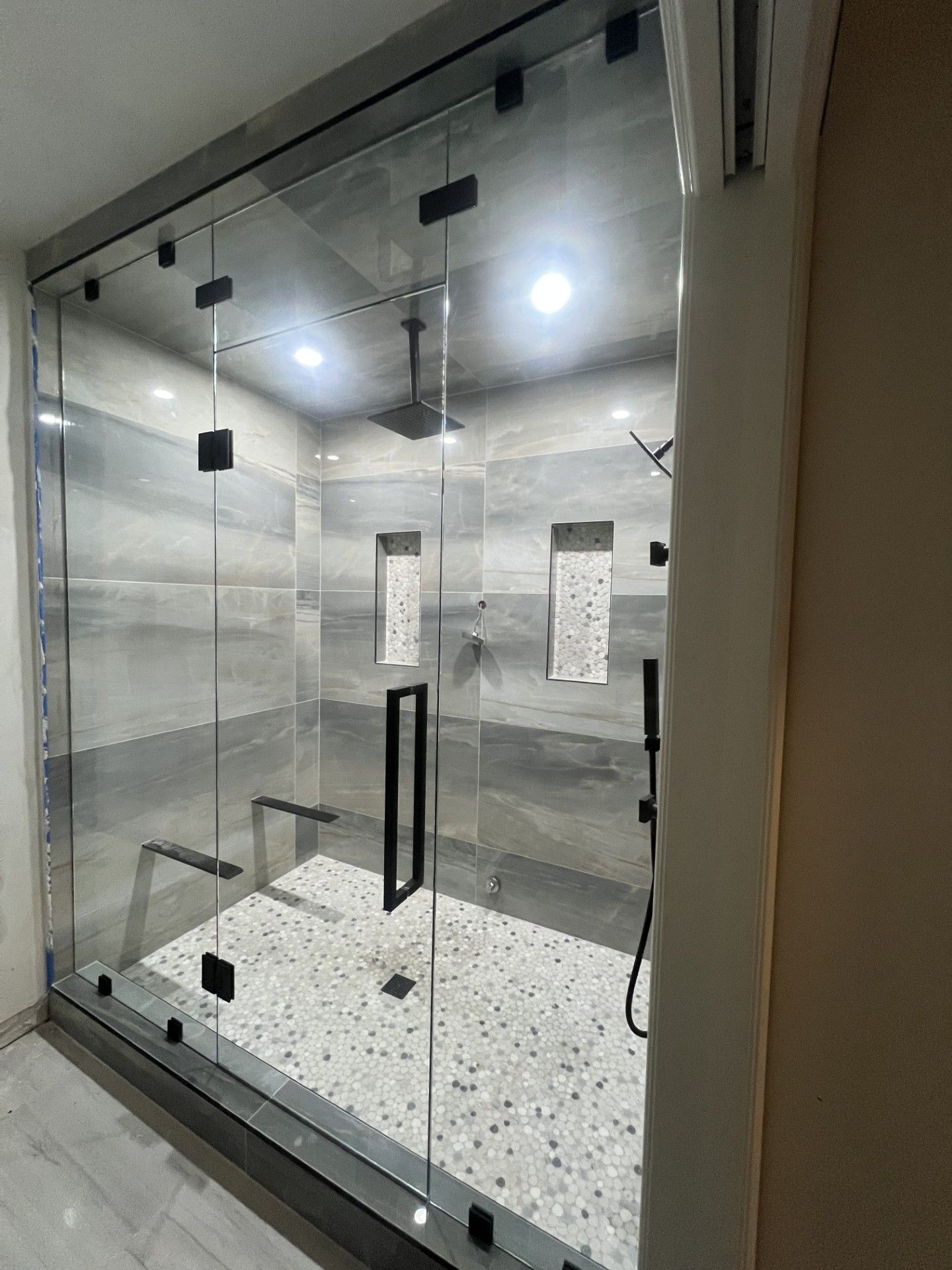 Glass-enclosed shower with a door, dark fixtures, and light-colored tile. Steam shower. Northville