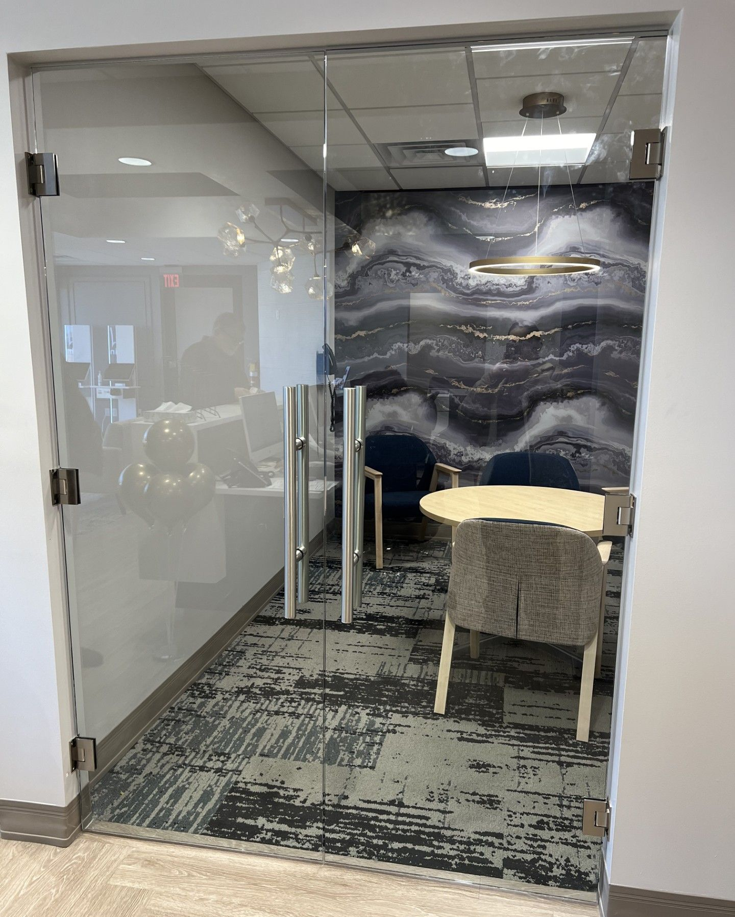Glass-walled office with patterned wall, table, and chairs. Door on left open.