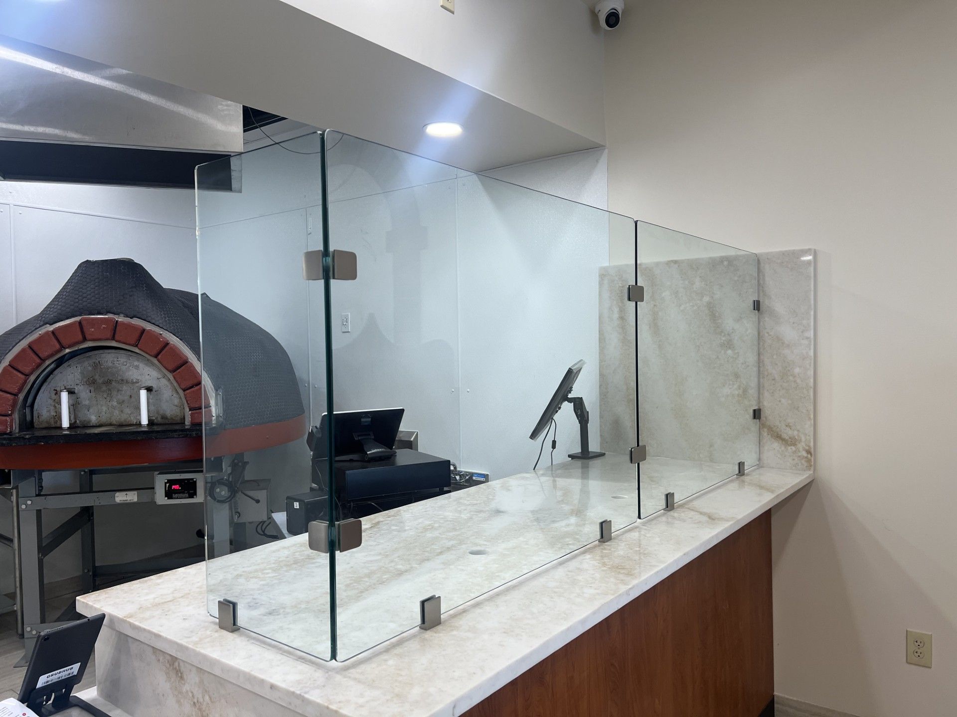 Glass barrier at a restaurant counter with a pizza oven visible in the background. Detroit