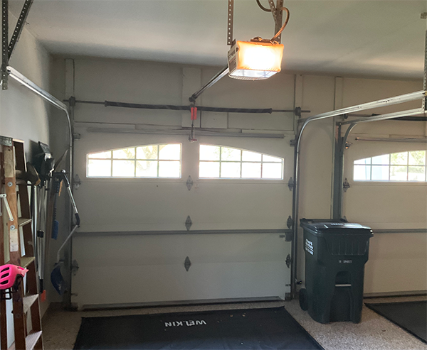 Garage interior with closed white door, overhead light, and two trash bins