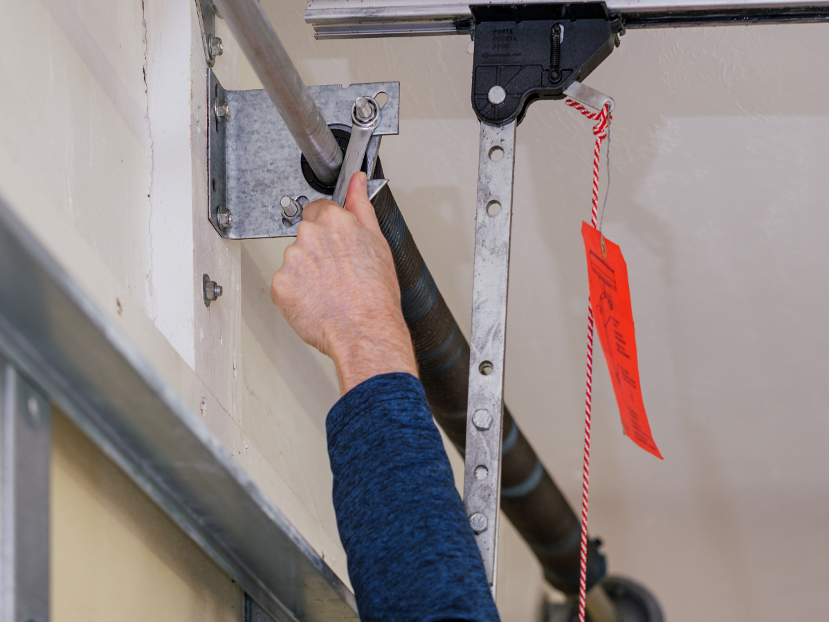 Hand adjusting a garage door opener chain on a ceiling rail, with a red pull tag nearby