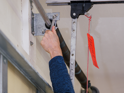 Hand reaching up to adjust a garage door opener mechanism with red pull cord visible