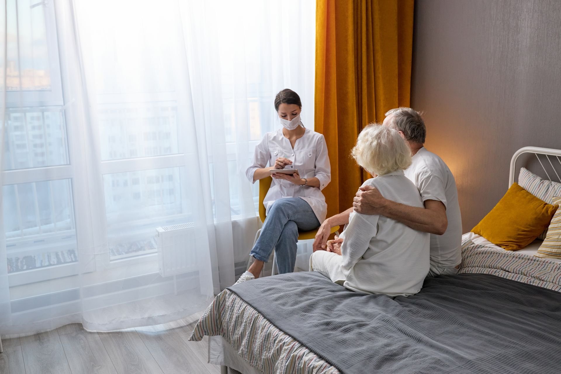 A nurse is talking to an elderly couple sitting on a bed.