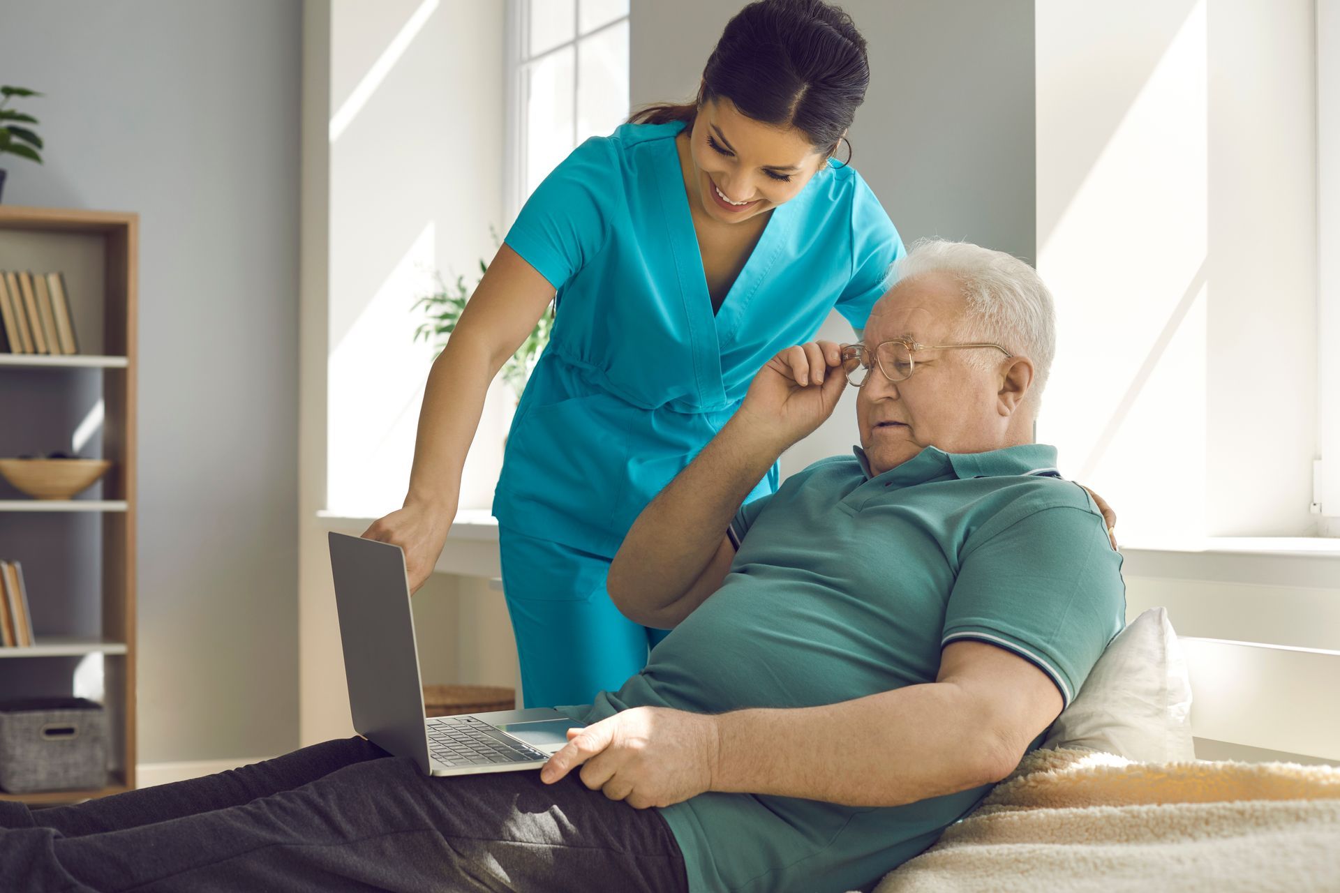 A nurse is helping an elderly man use a laptop computer.