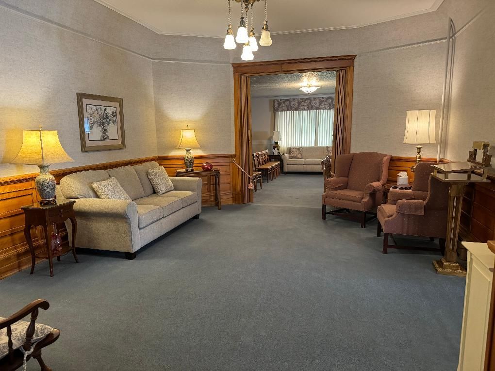 A formal sitting area with a sofa, two armchairs, side tables with lamps, blue carpeting, and an arched entryway.