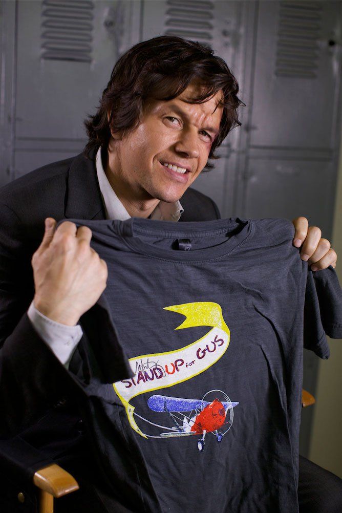 Actor, Mark Wahlberg, holding up a shirt for Jason Patric's non-profit, Stand Up for Gus.