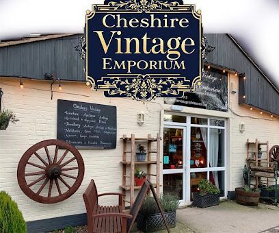 The storefront of Cheshire Vintage Emporium, a light-colored brick building with a large wooden wheel, bench, and plants.