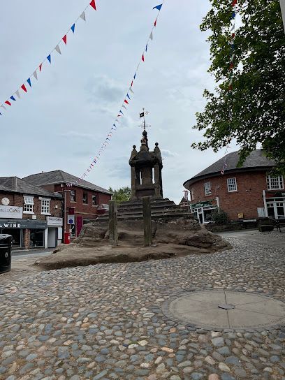 A stone monument on a cobblestone plaza in a town square, decorated with colorful bunting under a cloudy sky.
