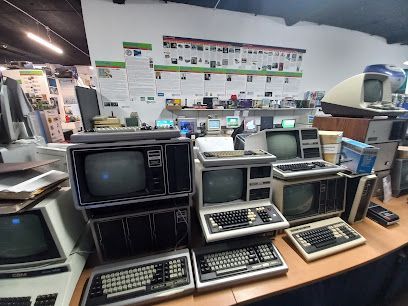 A desk filled with vintage computers and monitors in a museum-like setting, with informational posters on the wall.