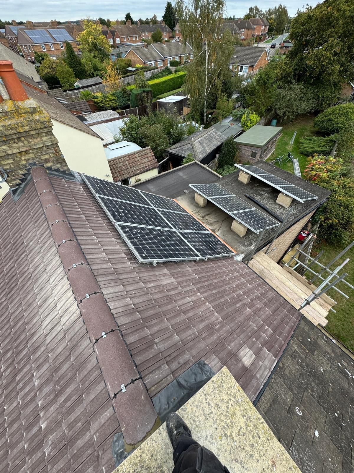 A high-angle view of a tiled residential roof with solar panels installed, overlooking a suburban neighborhood.