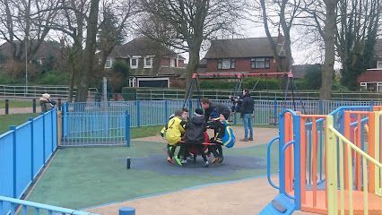 A group of people sitting together on a circular playground roundabout in an outdoor park setting.