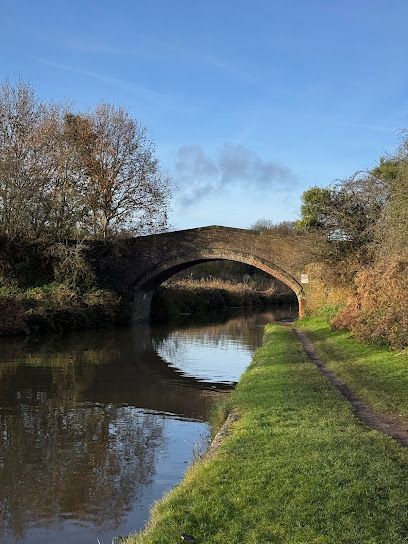 A stone arched bridge spans a calm canal, surrounded by autumn trees under a clear blue sky.