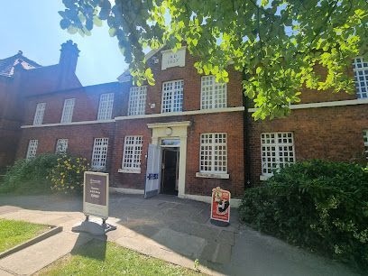 A red brick building with white-framed windows, an open entrance, and two informational signs on a sunny day.