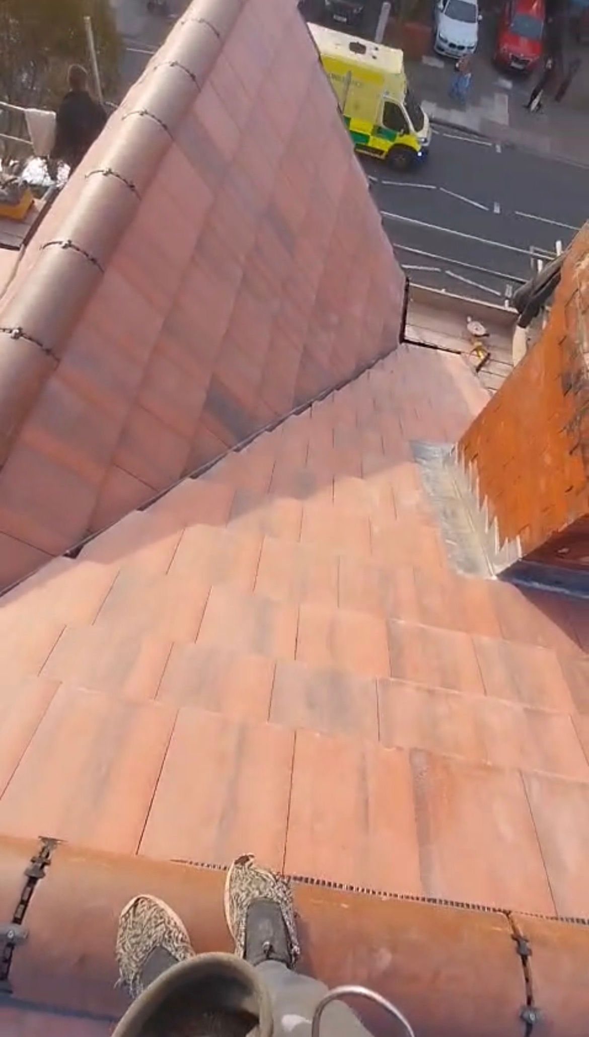 First-person perspective looking down at a terracotta tiled roof from a high vantage point, with a street visible below.