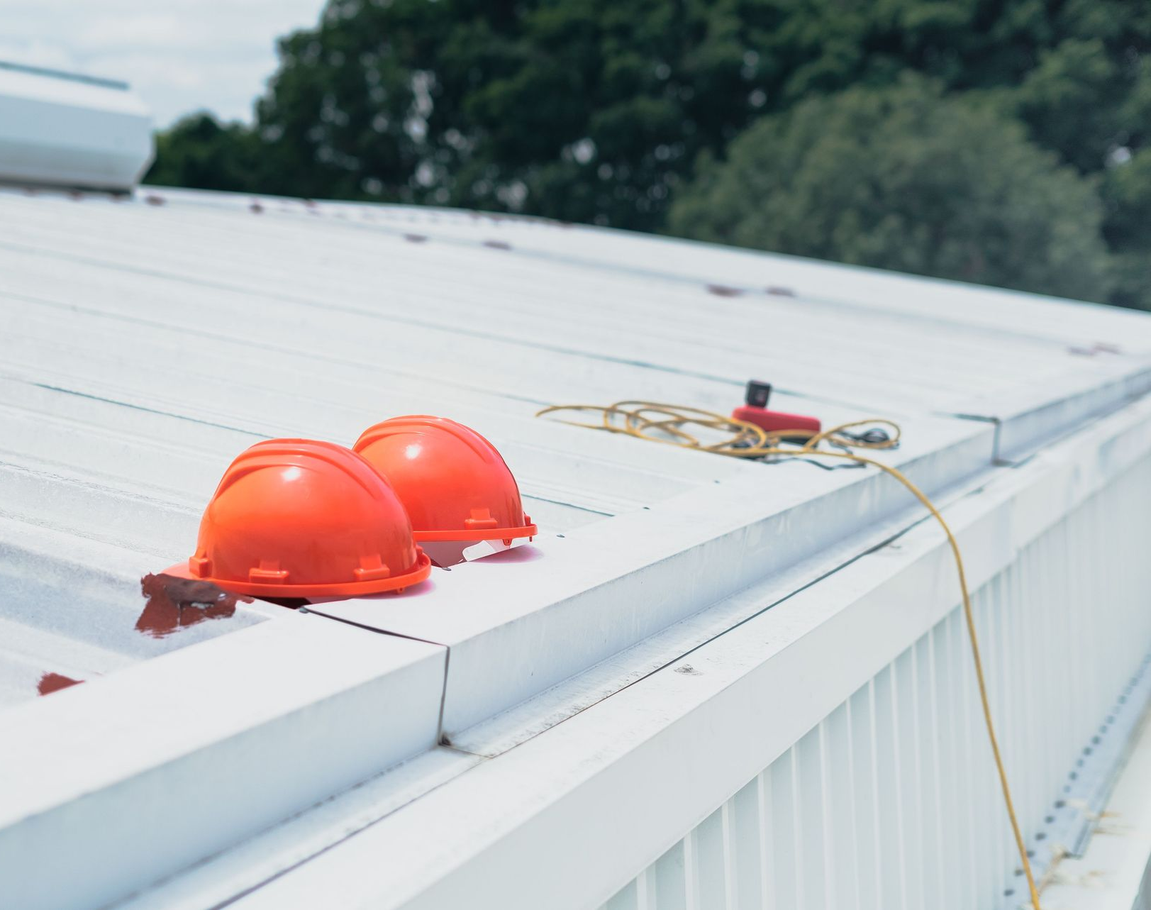 Two orange hard hats on a white industrial roof with safety rope attached
