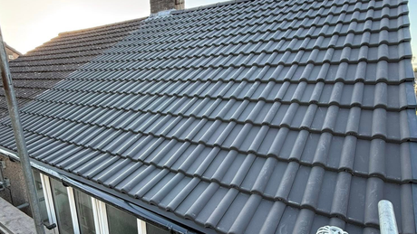 Dark grey resin driveway leading to a white garage door, flanked by gardens with greenery.