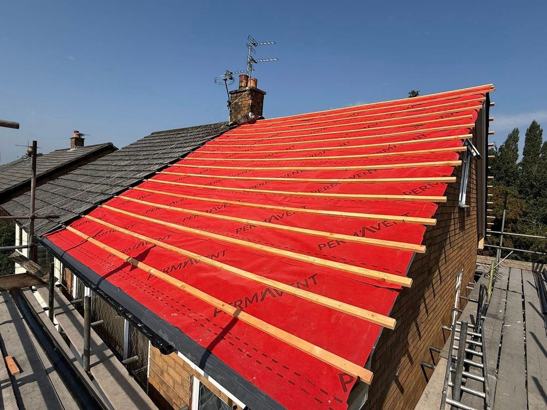 A partially renovated roof with bright red underlay and wooden battens installed, next to an old tiled roof.