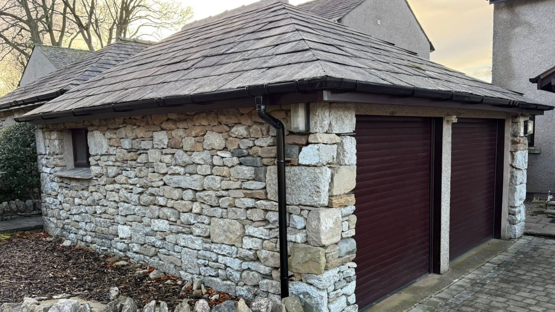 Dark grey resin driveway leading to a white garage door, flanked by gardens with greenery.