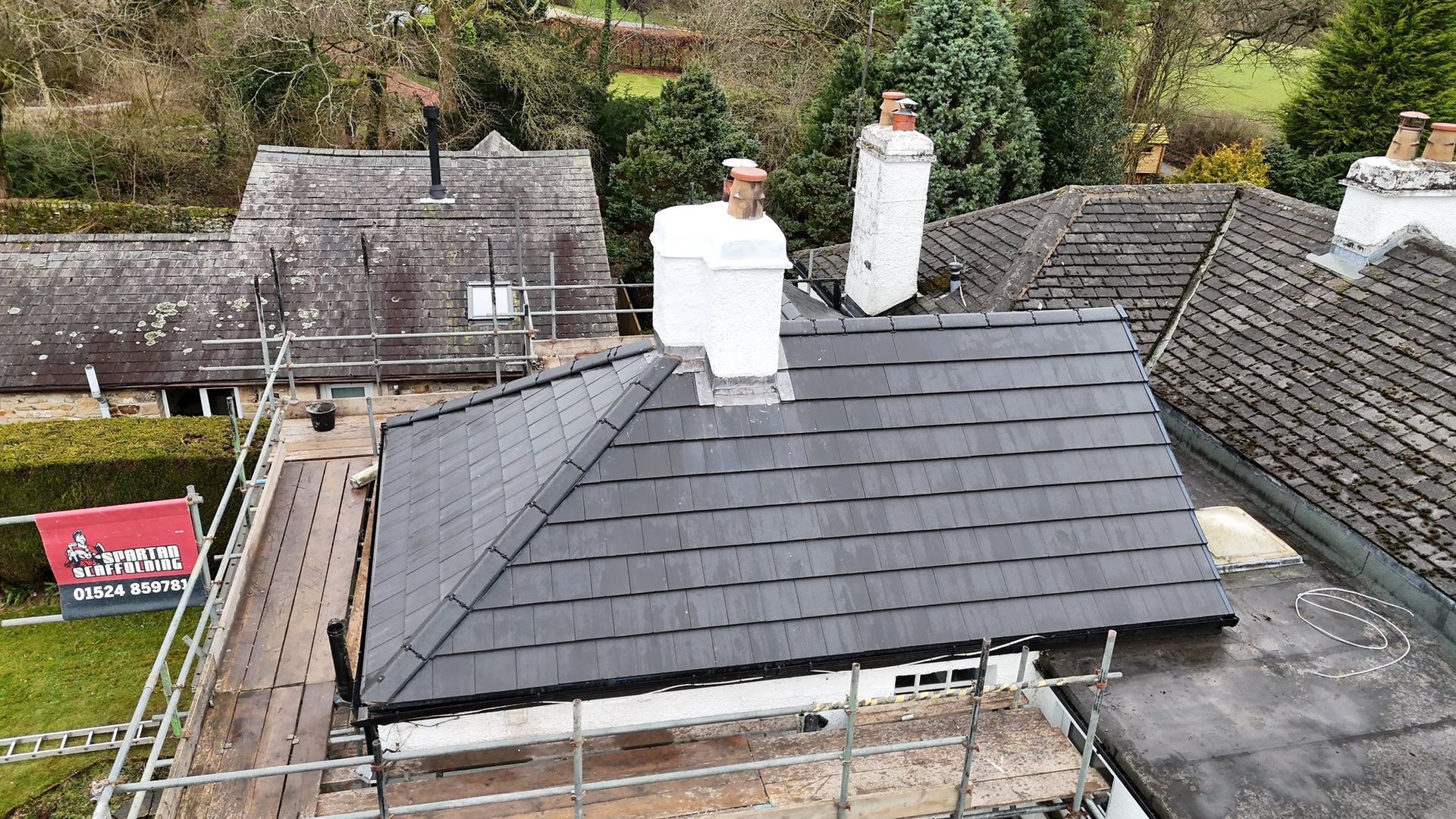 Grey resin driveway with light-colored buildings, dark car, and a wall in the background.