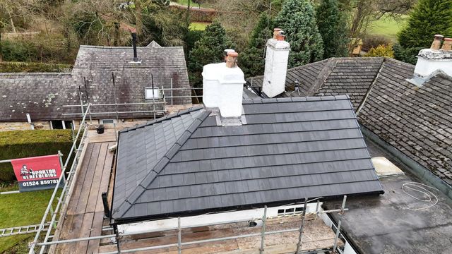 Grey resin driveway with light-colored buildings, dark car, and a wall in the background.