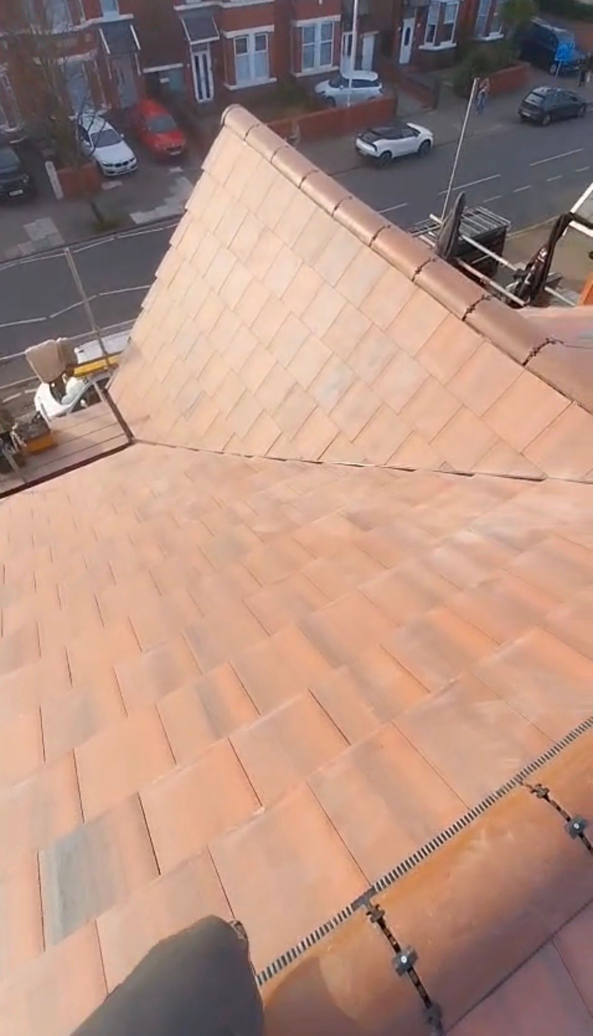A high-angle view of a newly tiled terracotta roof with a street and parked cars visible in the background.
