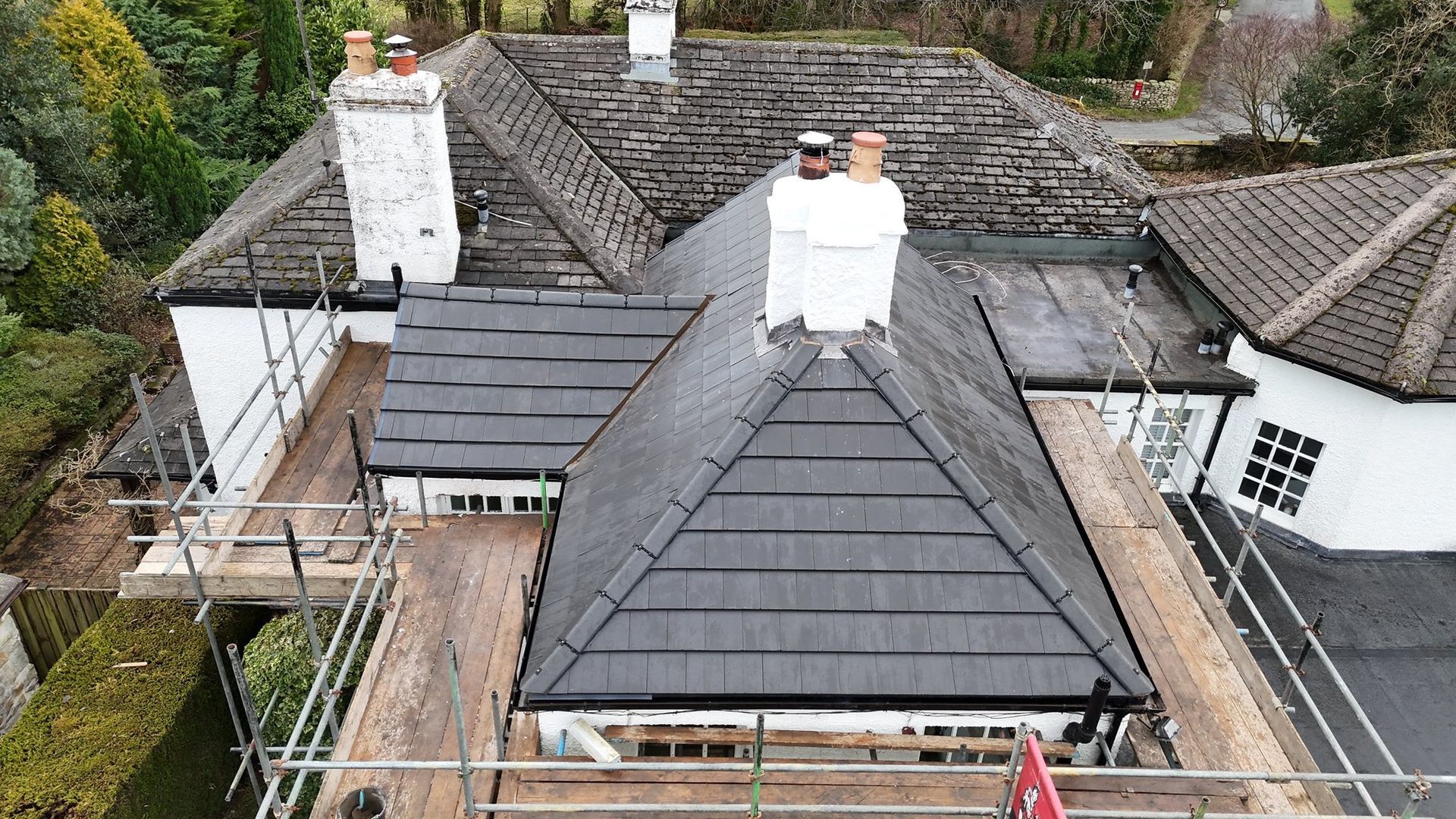 Aerial view of a two-story house with a resin bound driveway, green lawn, and surrounding trees.