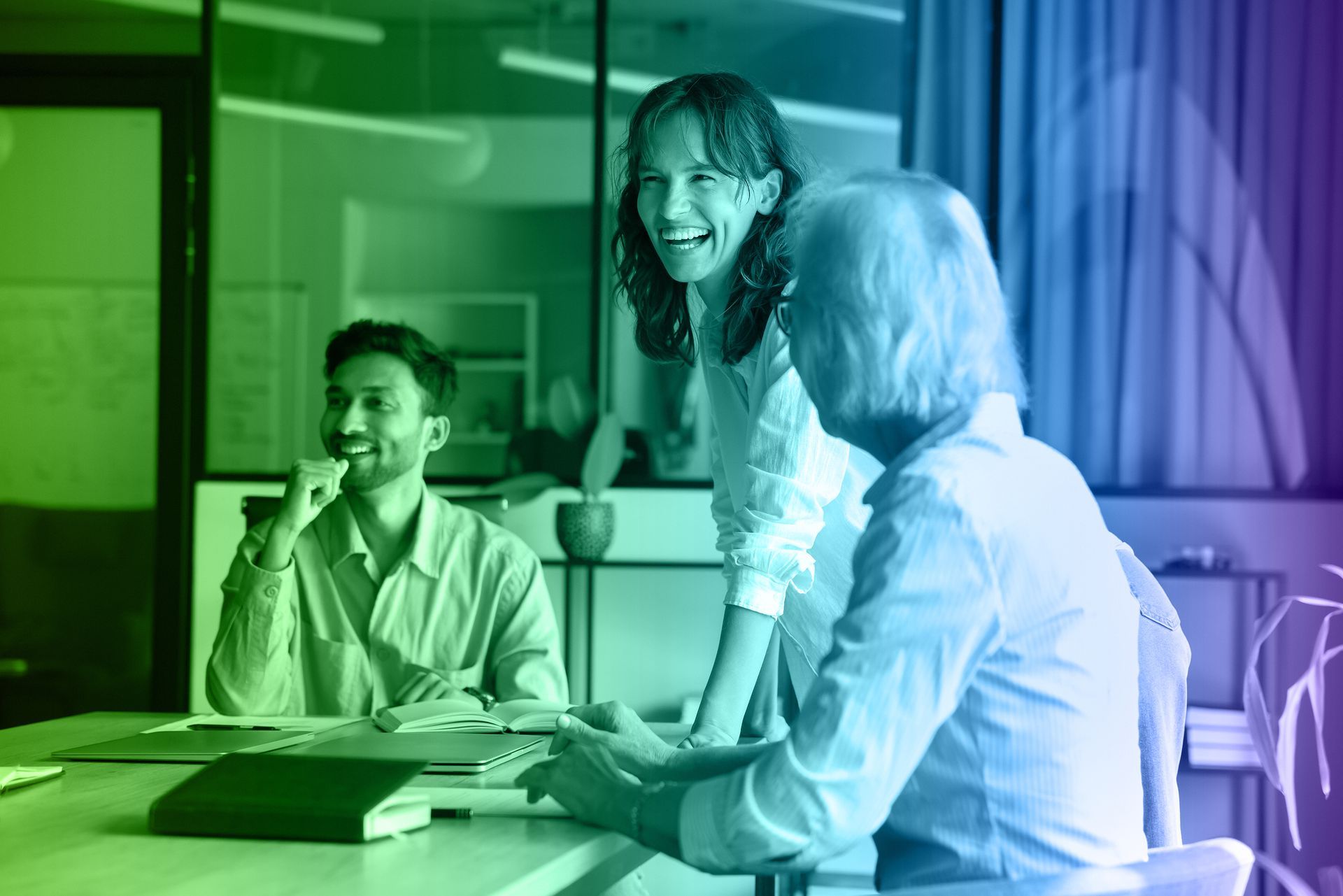Three people smiling around a table in an office. Green and blue color gradient overlay.