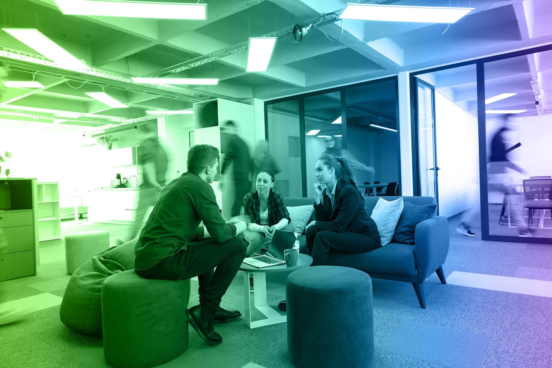 People conversing in a modern office lounge with colorful lighting and blurred movement in the background.