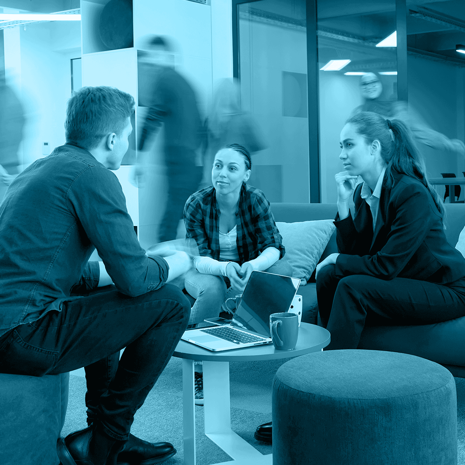Three people in casual discussion at a modern office, blurred figures in background.