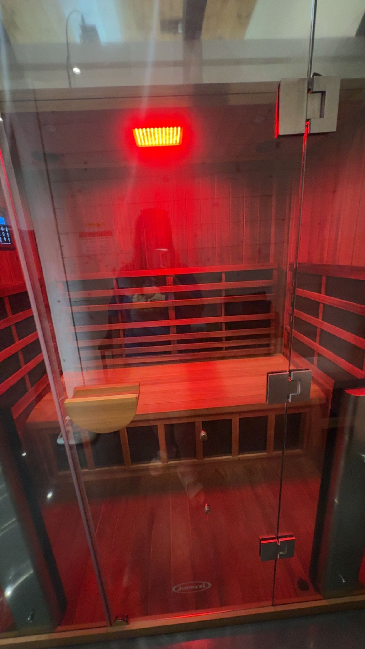 A wooden sauna with a glass door and a red light on the ceiling.