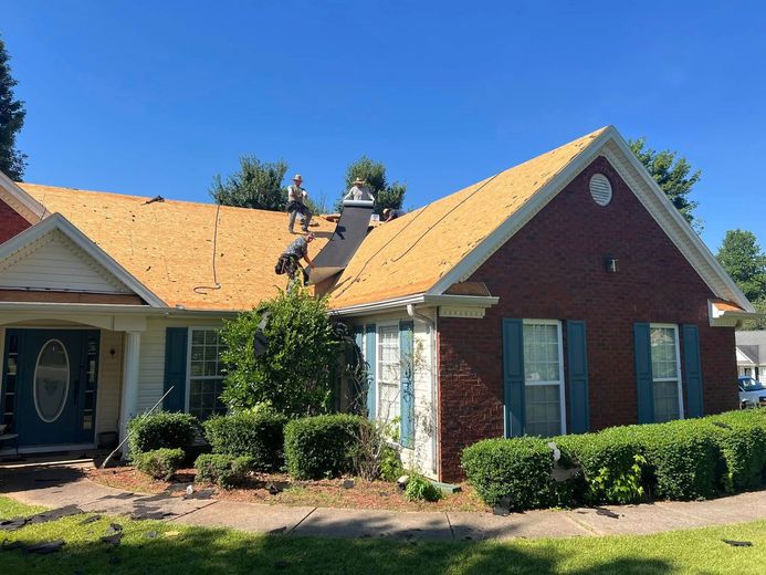 Roofers on a brick house removing old shingles under a blue sky.