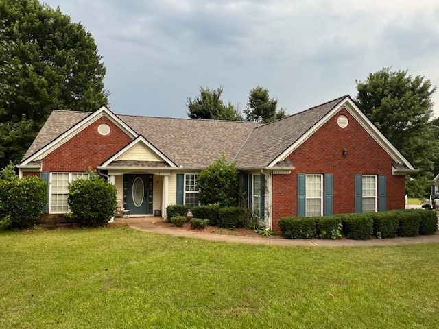 Brick ranch house with green shutters, lawn, and cloudy sky.