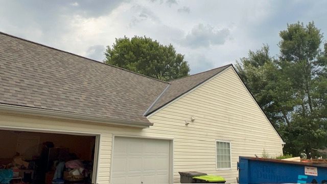 Tan house with garage, brown roof, and cream siding, under cloudy sky.