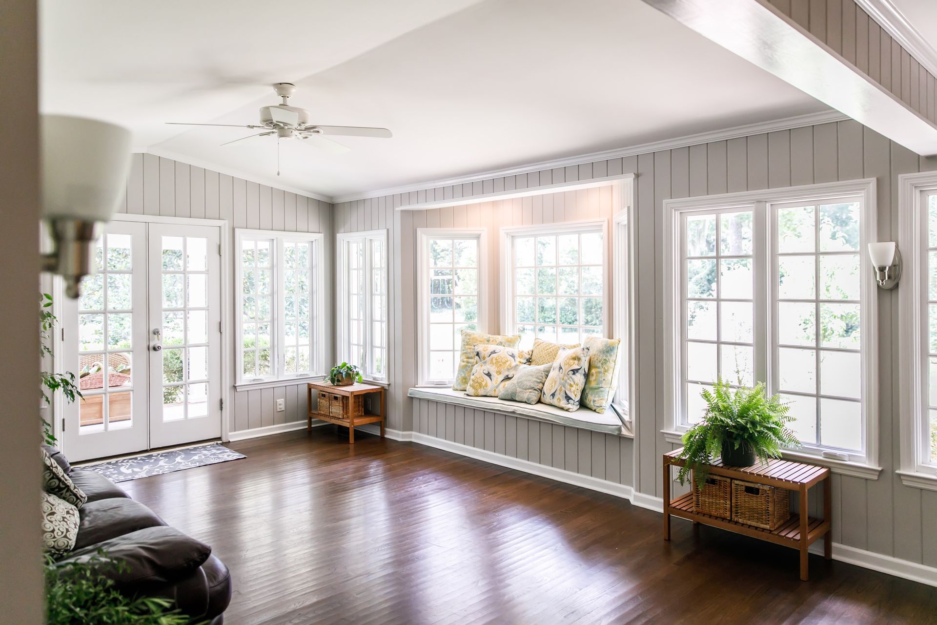 Sunroom with gray walls, dark wood floor, and a window seat with pillows.