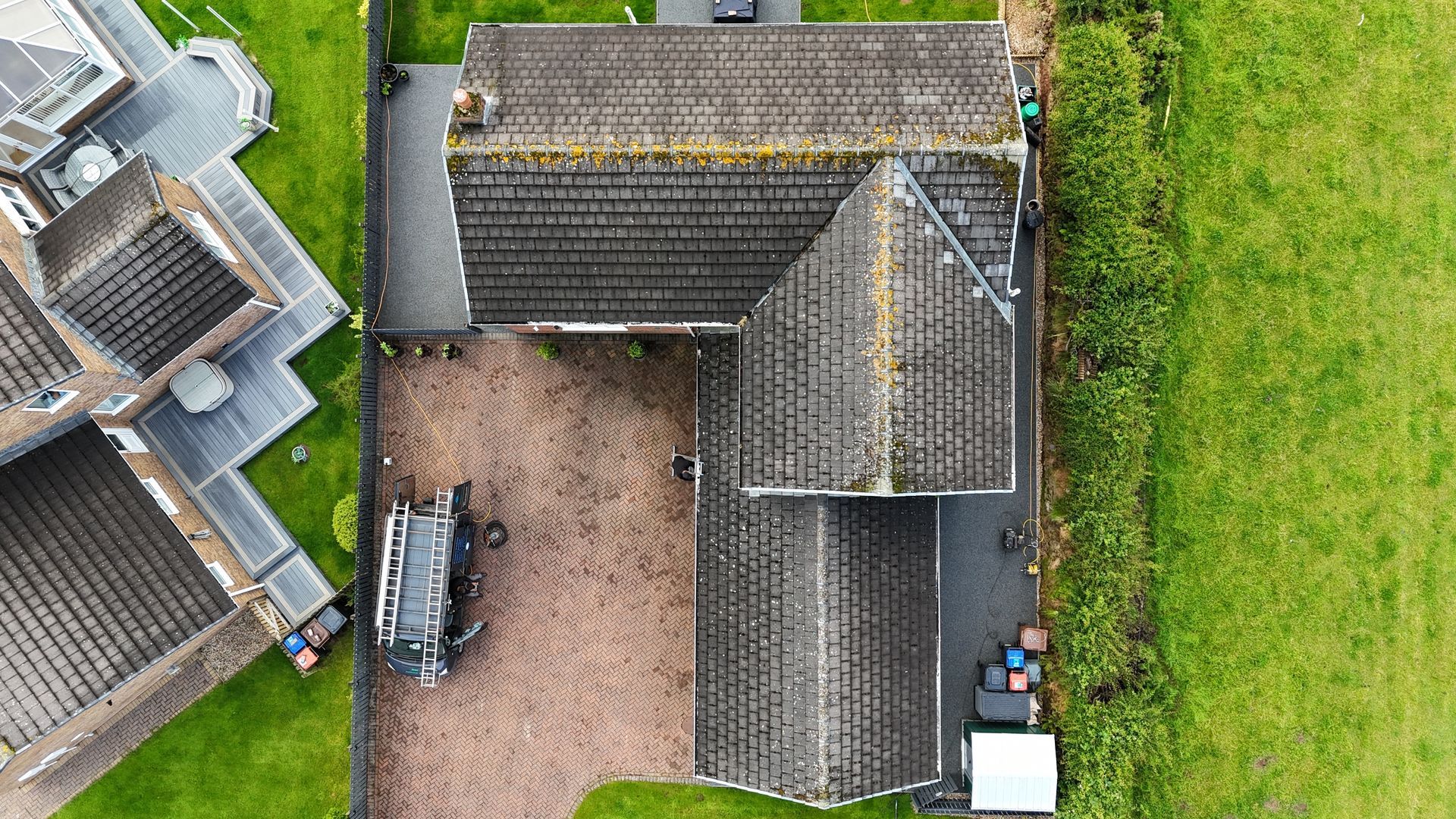 Overhead view of a house with a brown roof and driveway, next to green grass and a field.